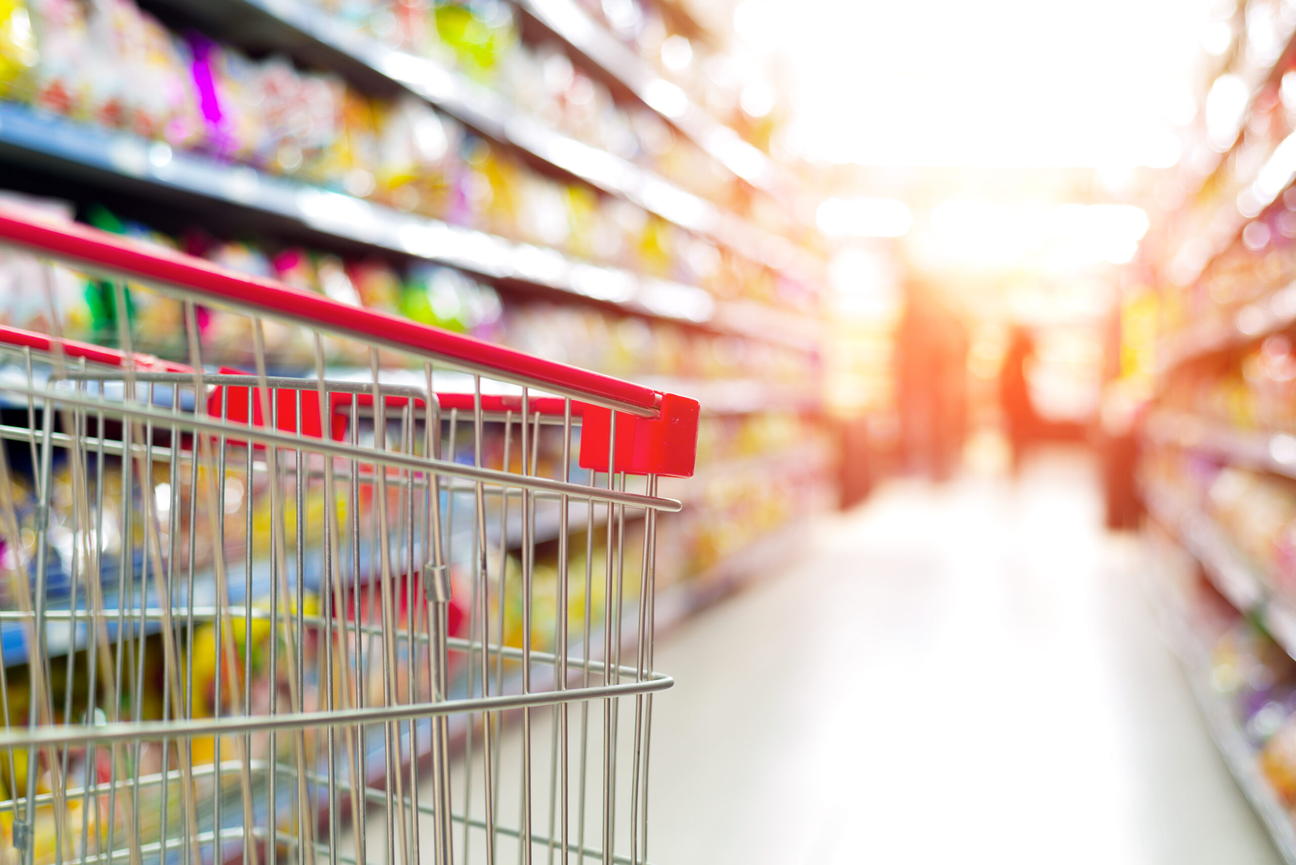 Supermarket interior, empty red shopping cart.